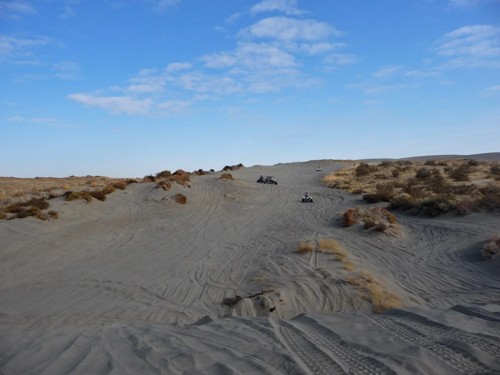 Ampia pista di sabbia tra dune e cespugli con piloti in lontananza